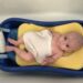first years sure comfort deluxe baby tub with baby inside of it with a sponge sling and shampo caddy